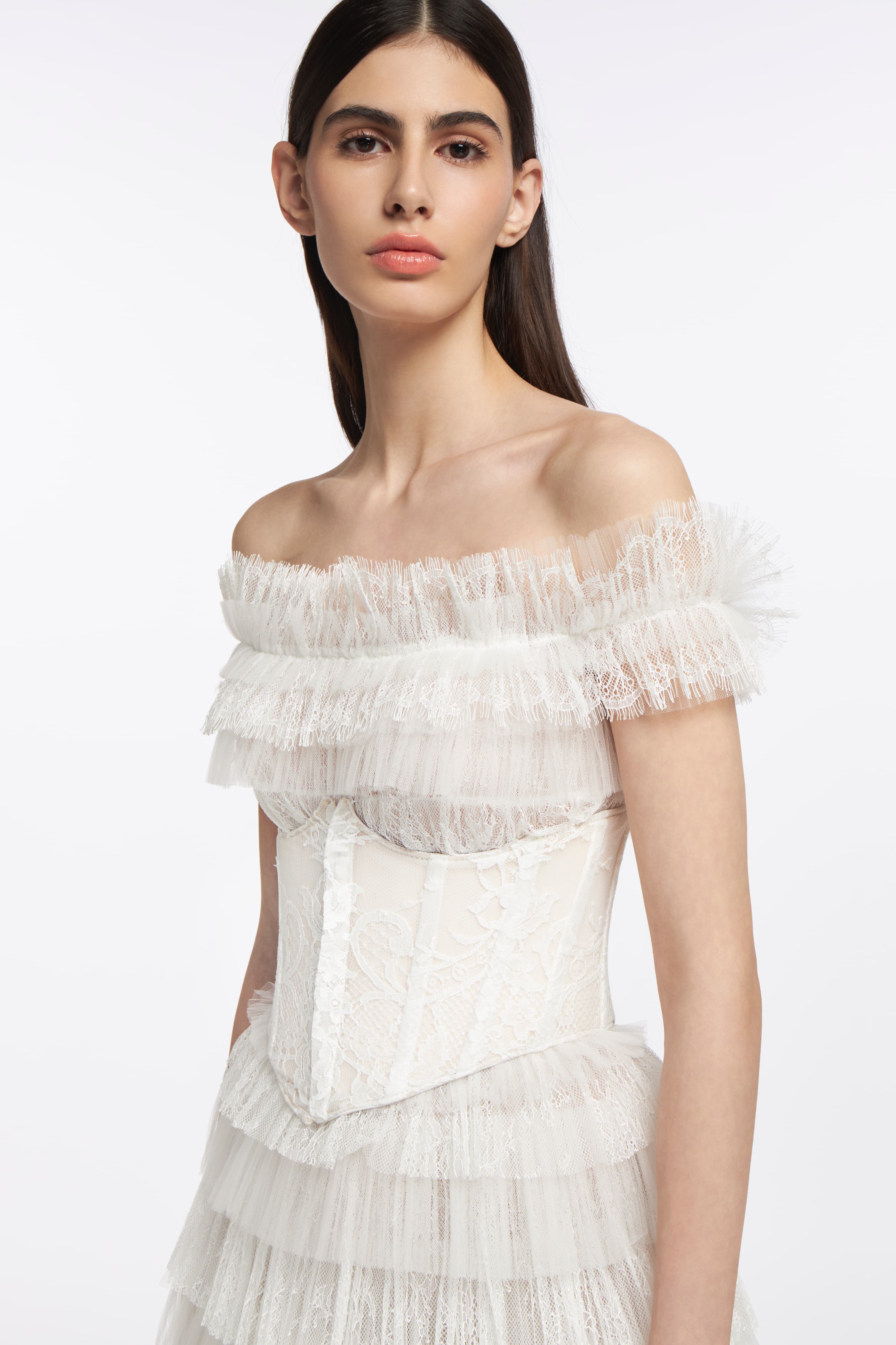 Amalthia Plissé Lace Gown styled with a lace corset, highlighting intricate detailing and an off-the-shoulder silhouette for a sophisticated bridal look.