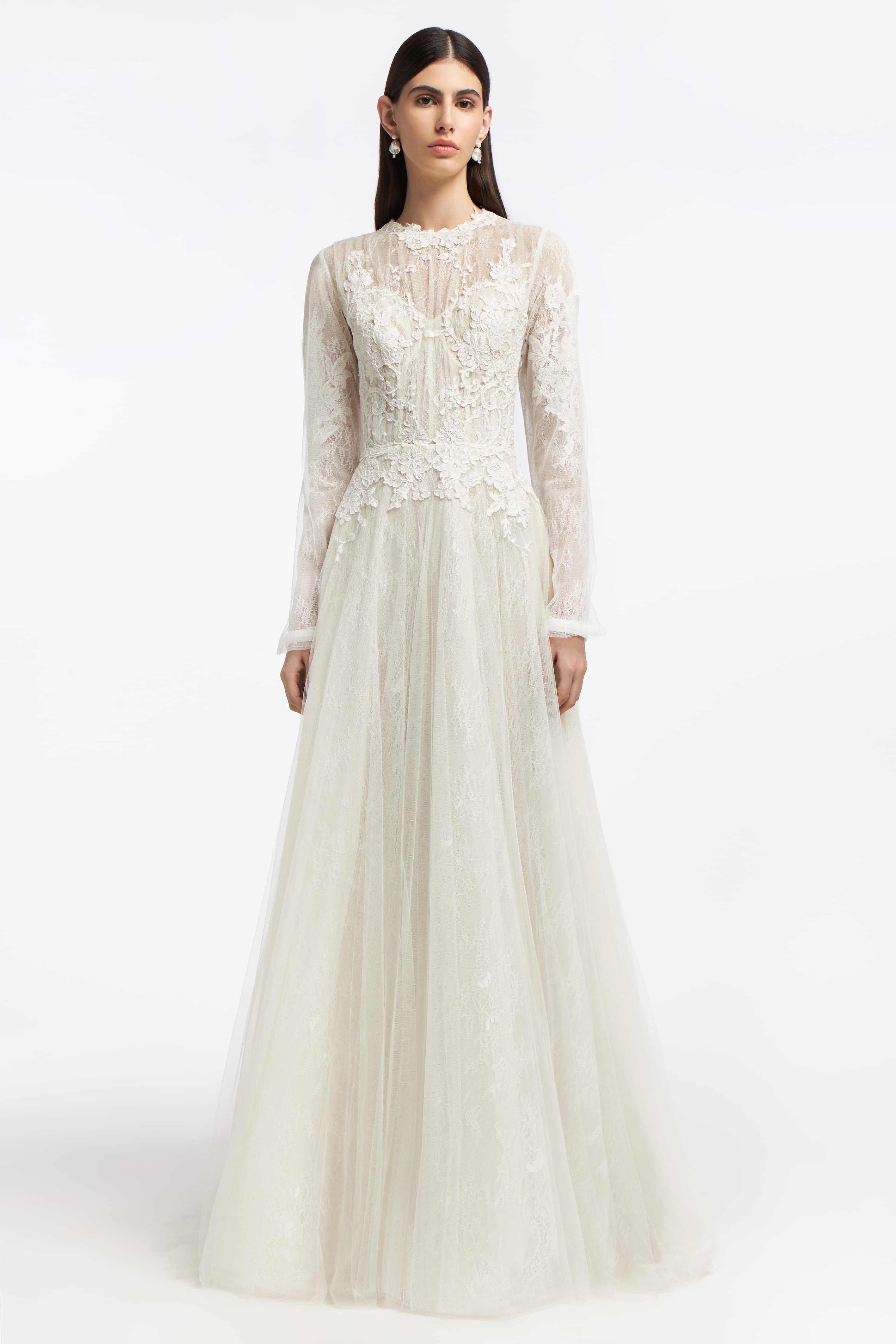 Elpis French Lace Gown featuring delicate floral lace, long sheer sleeves, and a flowing A-line silhouette. Perfect for a timeless bridal look.