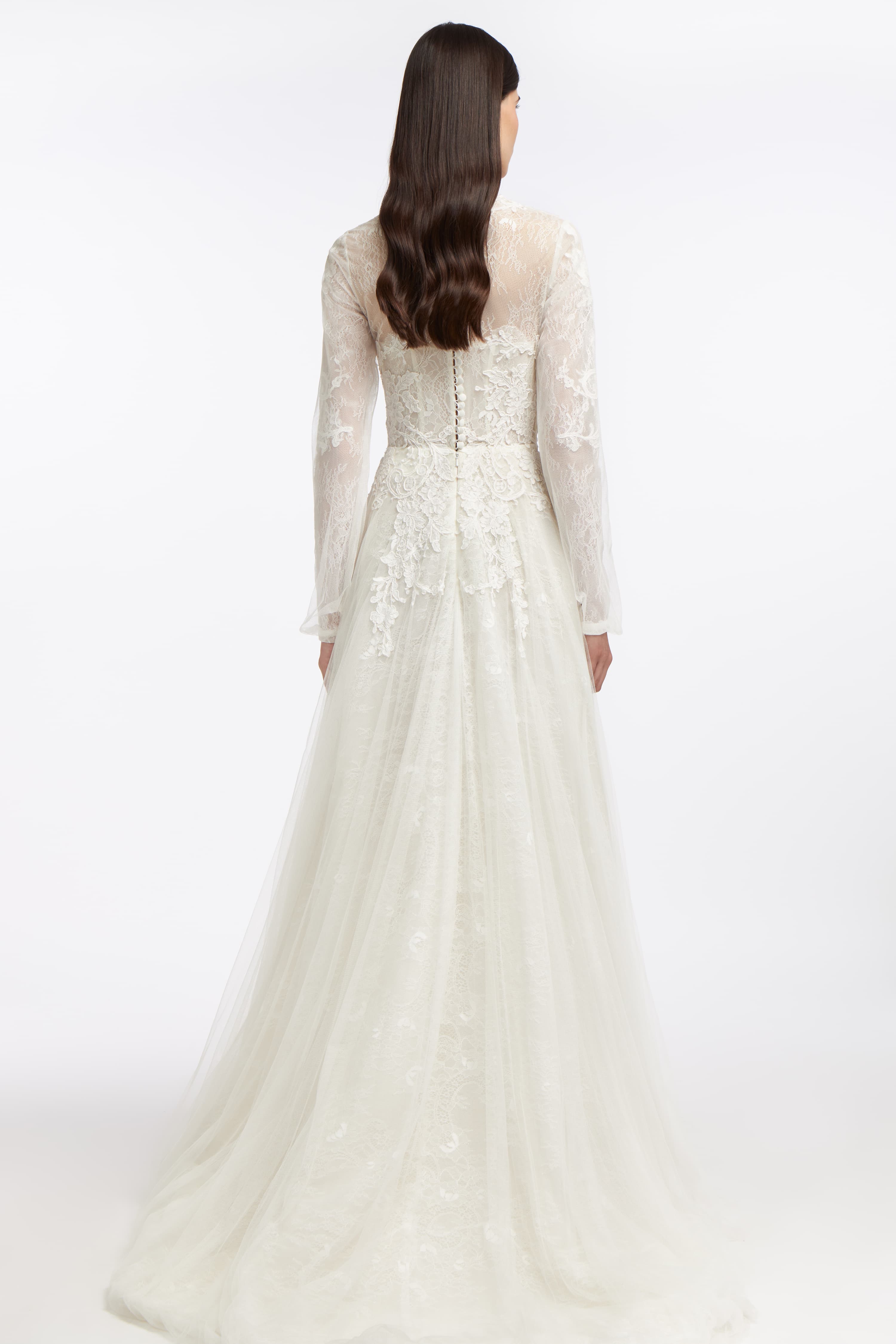 Back view of the Elpis French Lace Gown with sheer lace sleeves, button-up closure, and a flowing tulle train for a graceful wedding day look.