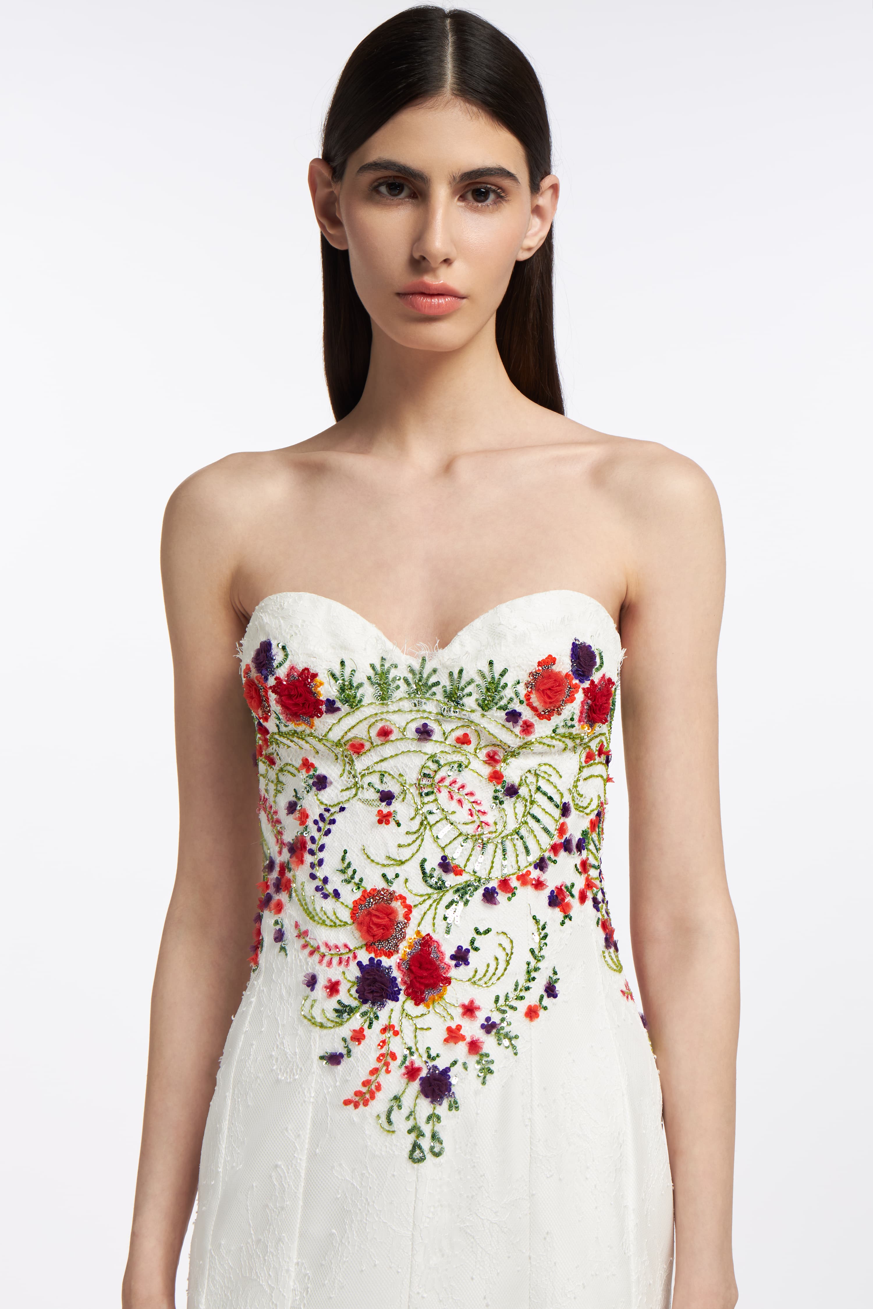 Close-up of the Melinoë Chantilly Lace Gown's bodice, showcasing vibrant floral embroidery on delicate white lace with a sweetheart neckline.