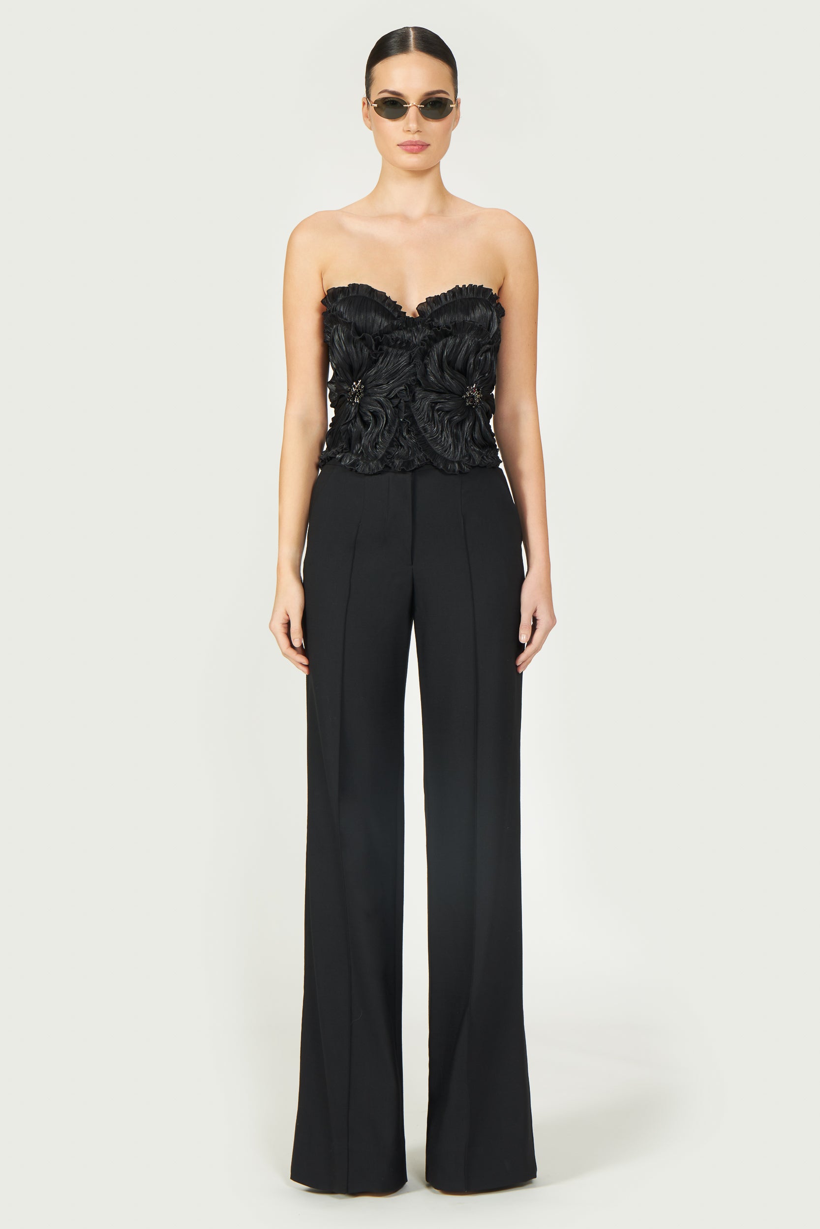 Model wearing Ezra Lurex Georgette Bustier, a black strapless top with ruffled floral accents. Perfect for elegant evening wear from Resort 2025.