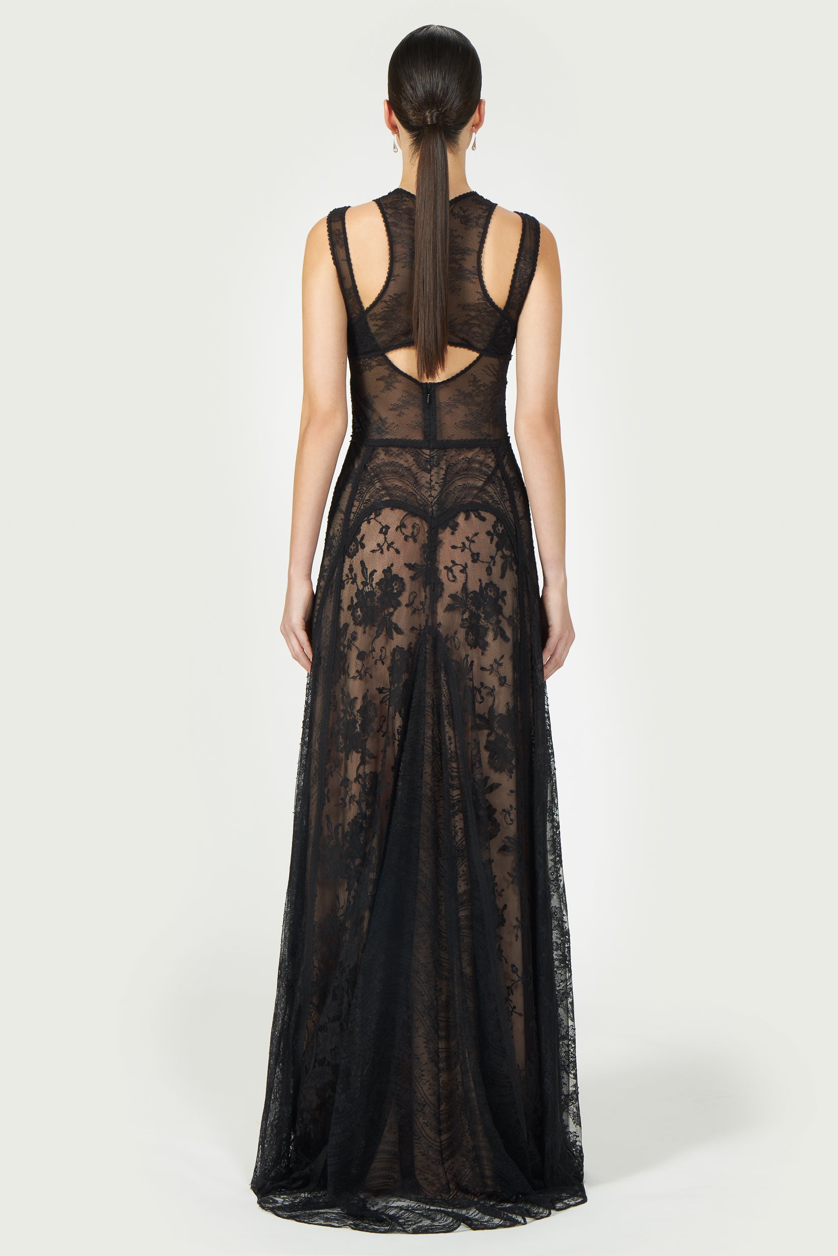 Back view of the Massima Patchwork Lace Gown featuring sheer lace panels, an open-back design, and a flowing floor-length silhouette.