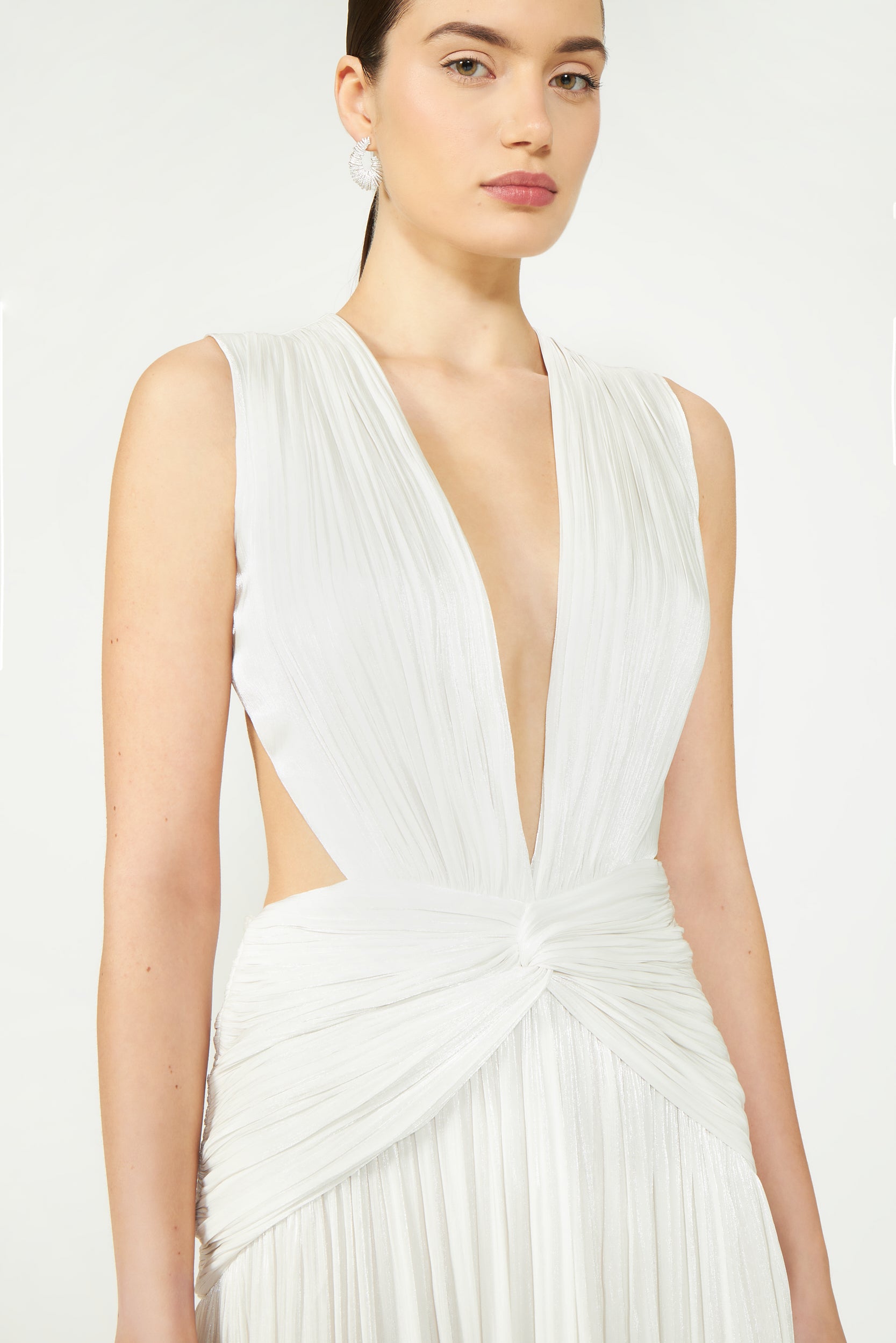 Elegant white sleeveless gown with deep V-neck, featuring pleated fabric and knotted waist detail.