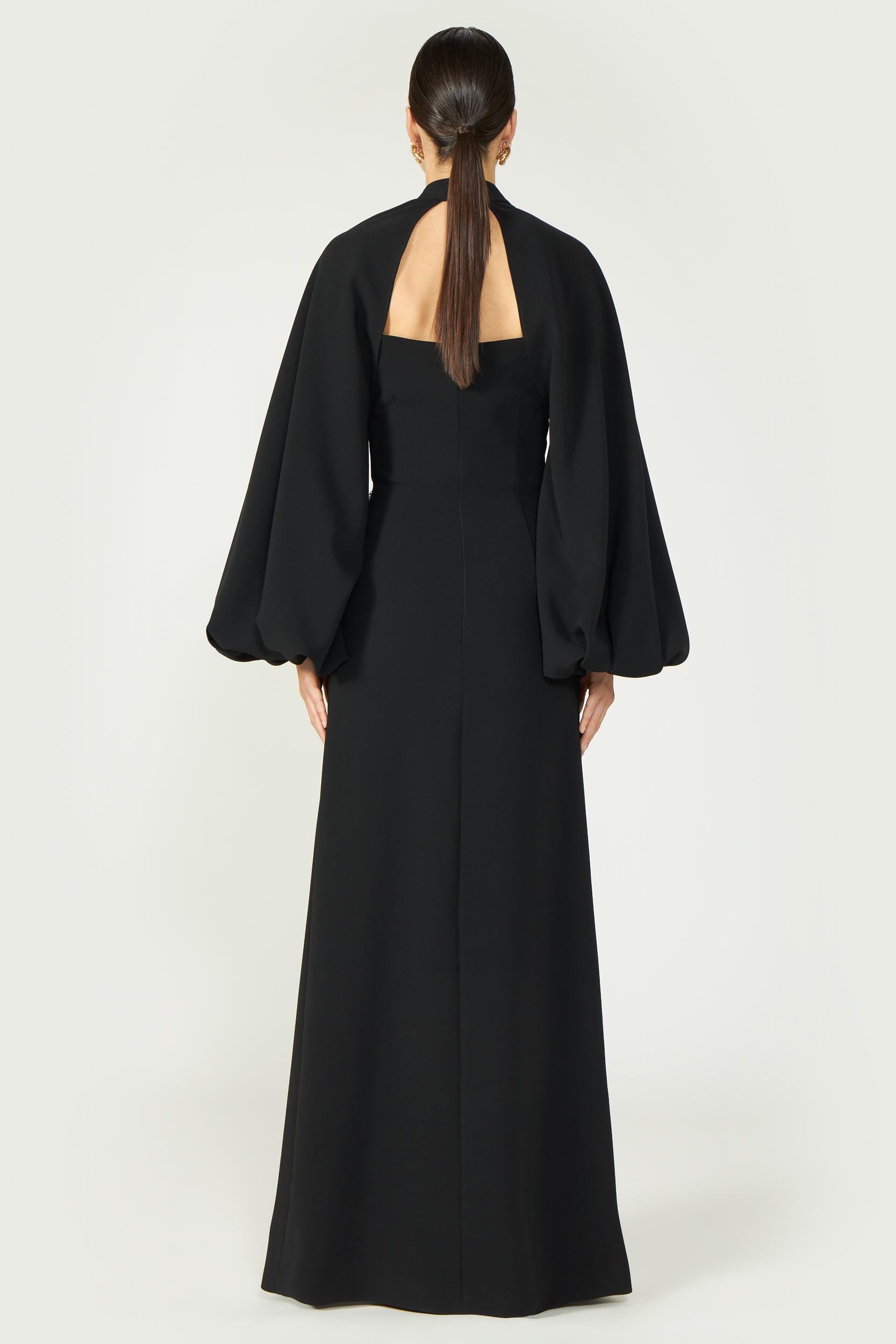 Back view of a long black gown with open back design and voluminous cape sleeves, ideal for elegant evening events.