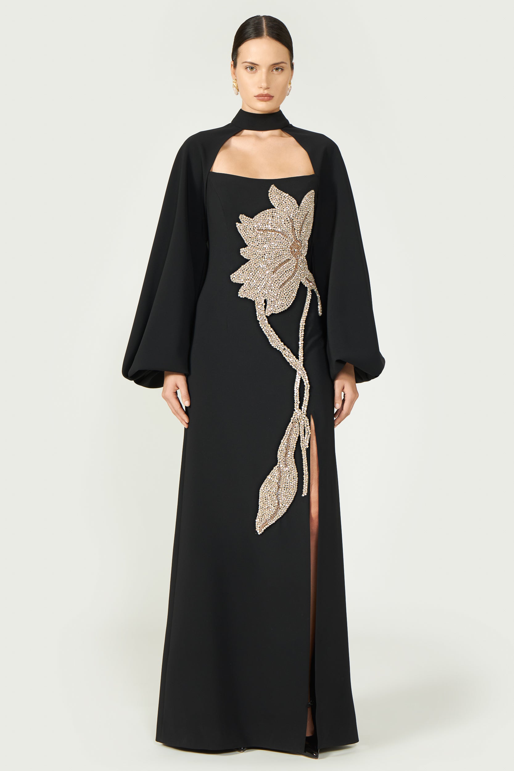 Elegant black evening gown with high-neck capelet and intricate gold floral embellishment, featuring a floor-length silhouette.