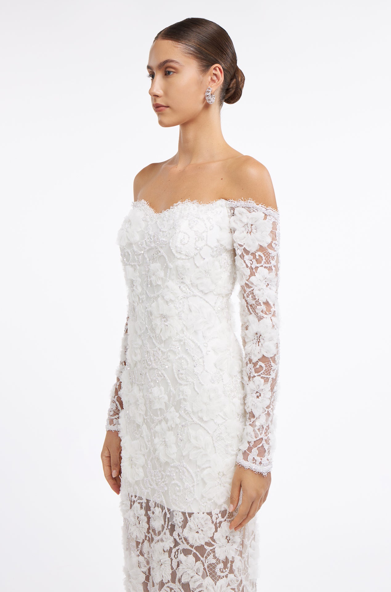 Side view of the Chrisanthi Embellished Lace Gown showcasing intricate floral lace details, off-the-shoulder design, and sheer long sleeves. Perfect for bridal elegance.