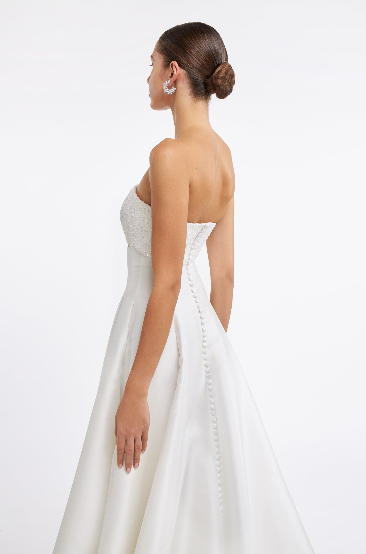Side view of the Cornilia Strapless Mikado Gown showcasing intricate beading, structured bodice, and buttoned back detail. Perfect for a modern bride.