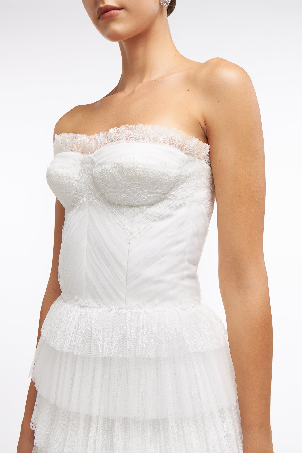 Close-up of the Ismene Plissé French Tulle Gown showcasing intricate lace detailing, structured bodice, and delicate ruffled trim for a romantic bridal look.