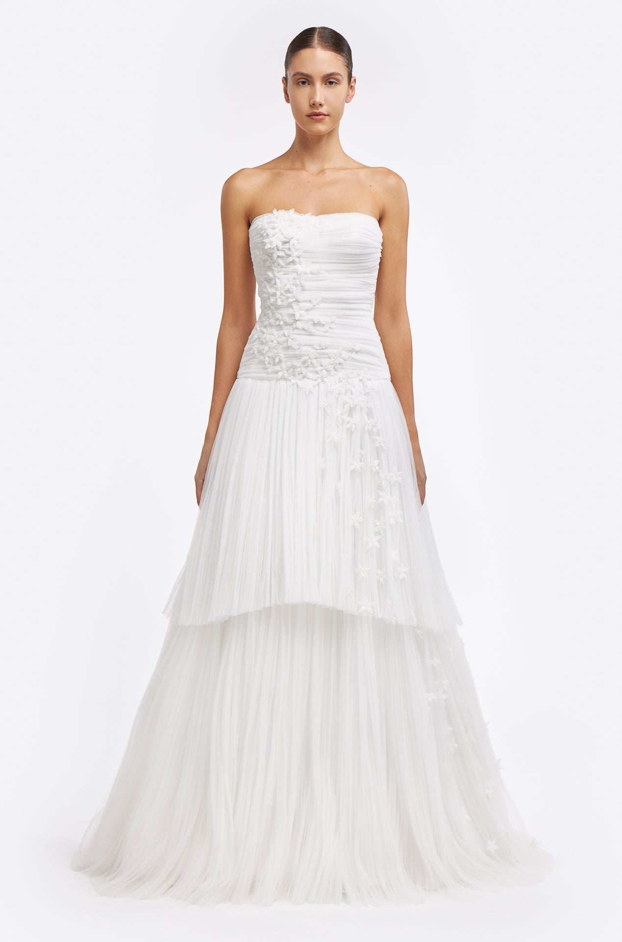 Zinovia Plissé French Tulle Gown featuring a strapless ruched bodice and layered tulle skirt with delicate floral appliqués. A timeless bridal look for Fall 2025.