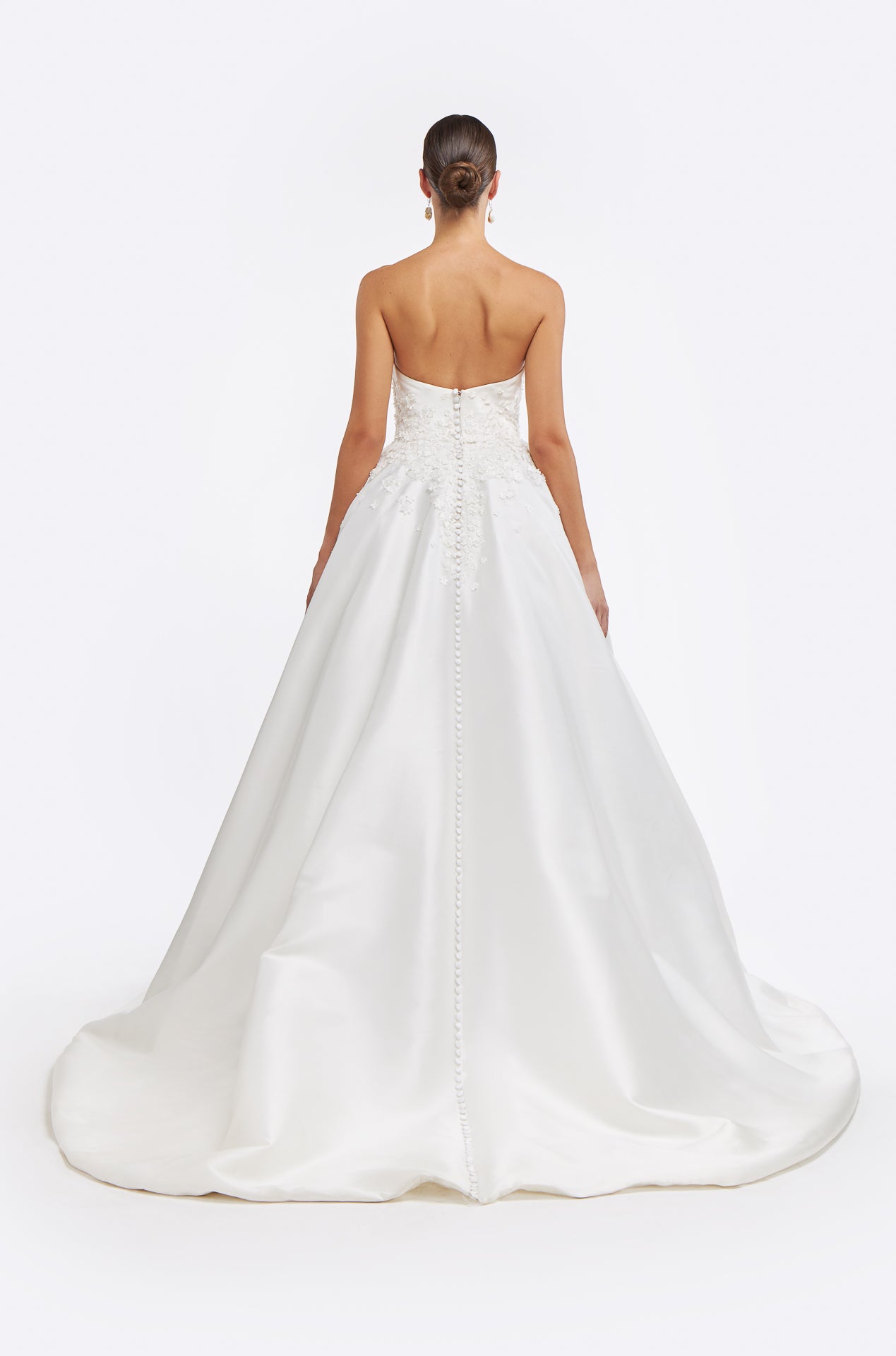 Back view of Vasia Mikado Strapless Gown with a flowing train and button detailing. A sophisticated bridal gown perfect for an elegant wedding.