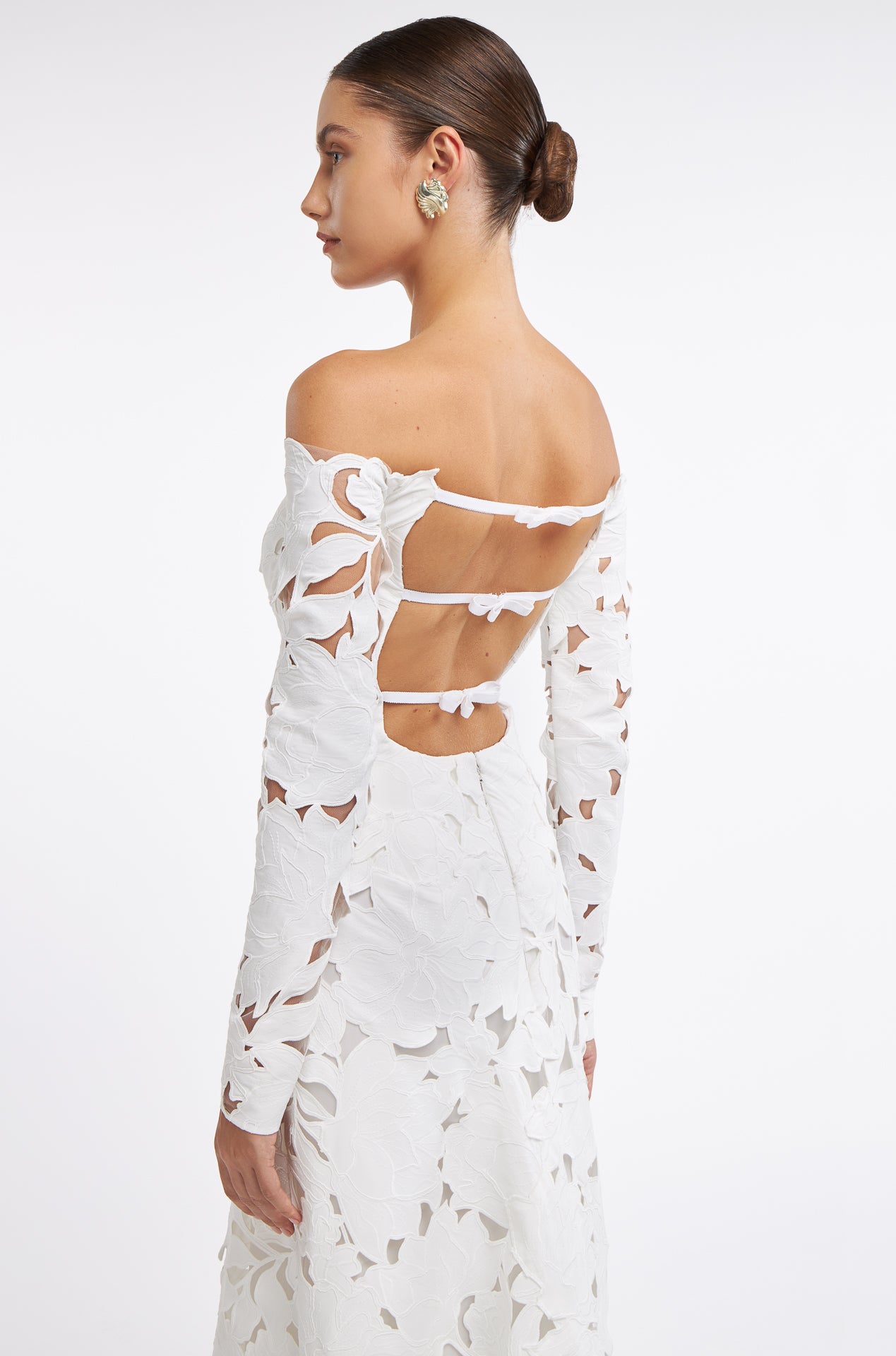 Side view of the Oriane Floral-Cut Lace Gown showcasing its open-back design with delicate strap details. The floral lace pattern enhances the gown's romantic appeal.